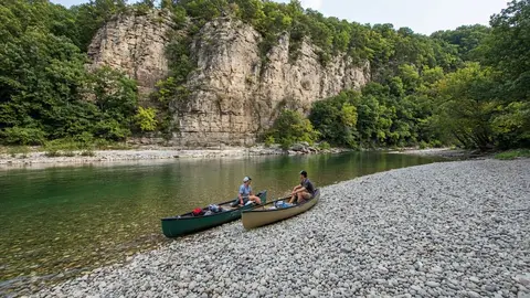 Canoes pulled up on a wide gravel bar below limestone bluffs