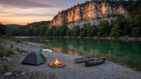Tent and campfire on a gravel bar at dusk with canoes tied off