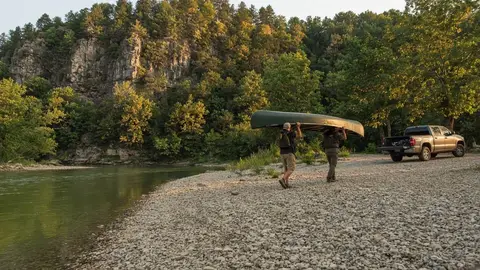 Paddlers carrying a canoe up a gravel bar to a parking area